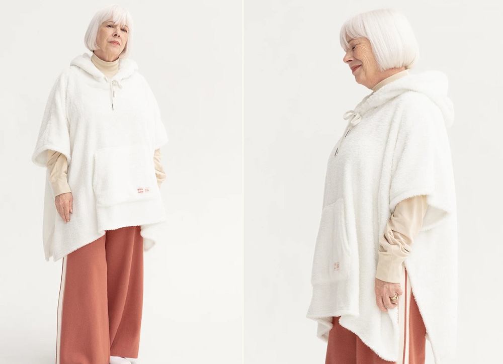 An elder white-haired woman wearing a white poncho blanket and brown pants on unhide's product page