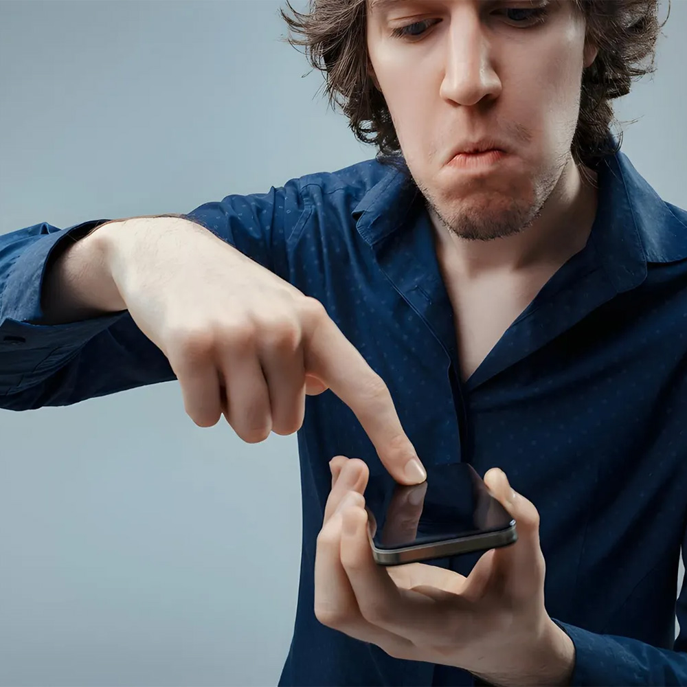Man with a confused expression pointing at his smartphone screen with one finger.