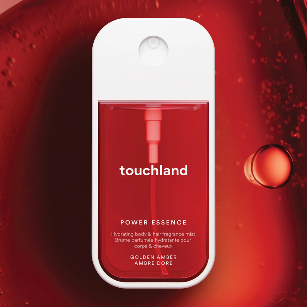 Touchland Power Essence hydrating body and hair fragrance mist, Golden Amber scent, in a red spray bottle against a red liquid background.