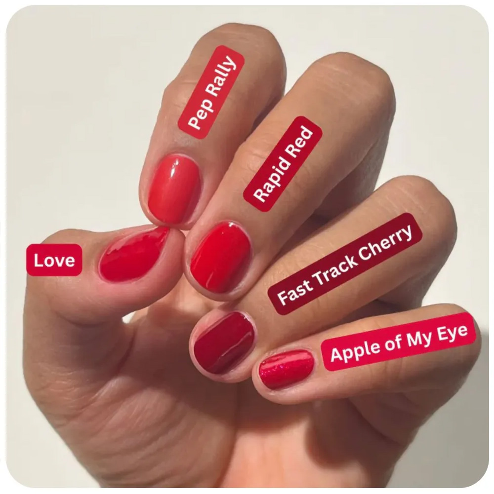 Hand with five different red nail polish shades labeled on each finger: Love, Pep Rally, Rapid Red, Fast Track Cherry, and Apple of My Eye.